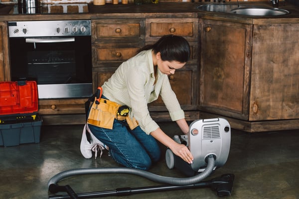 Attractive young repairwoman fixing vacuum cleaner on floor of kitchen