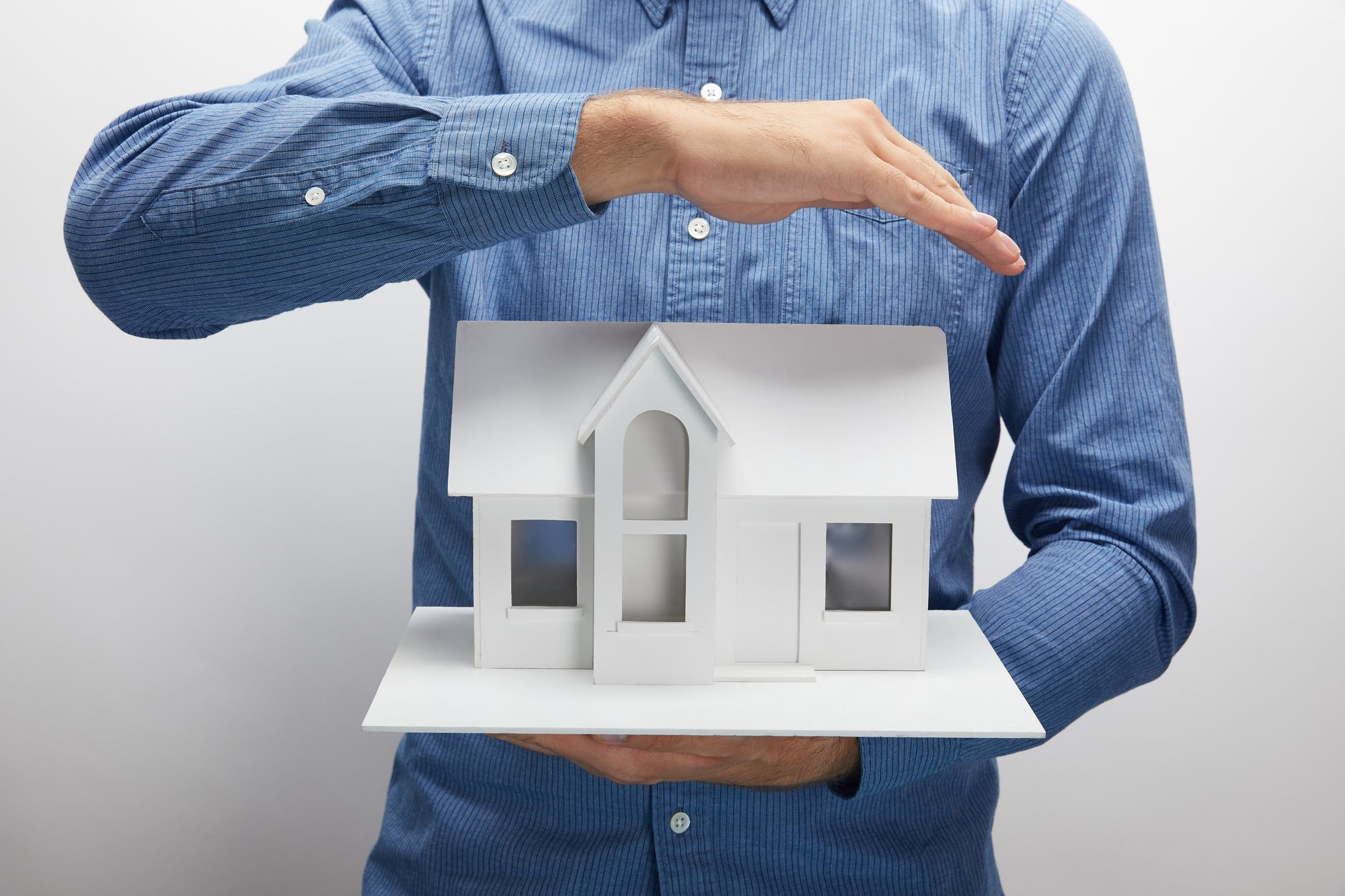 Cropped shot of man holding small house model on grey, insurance concept