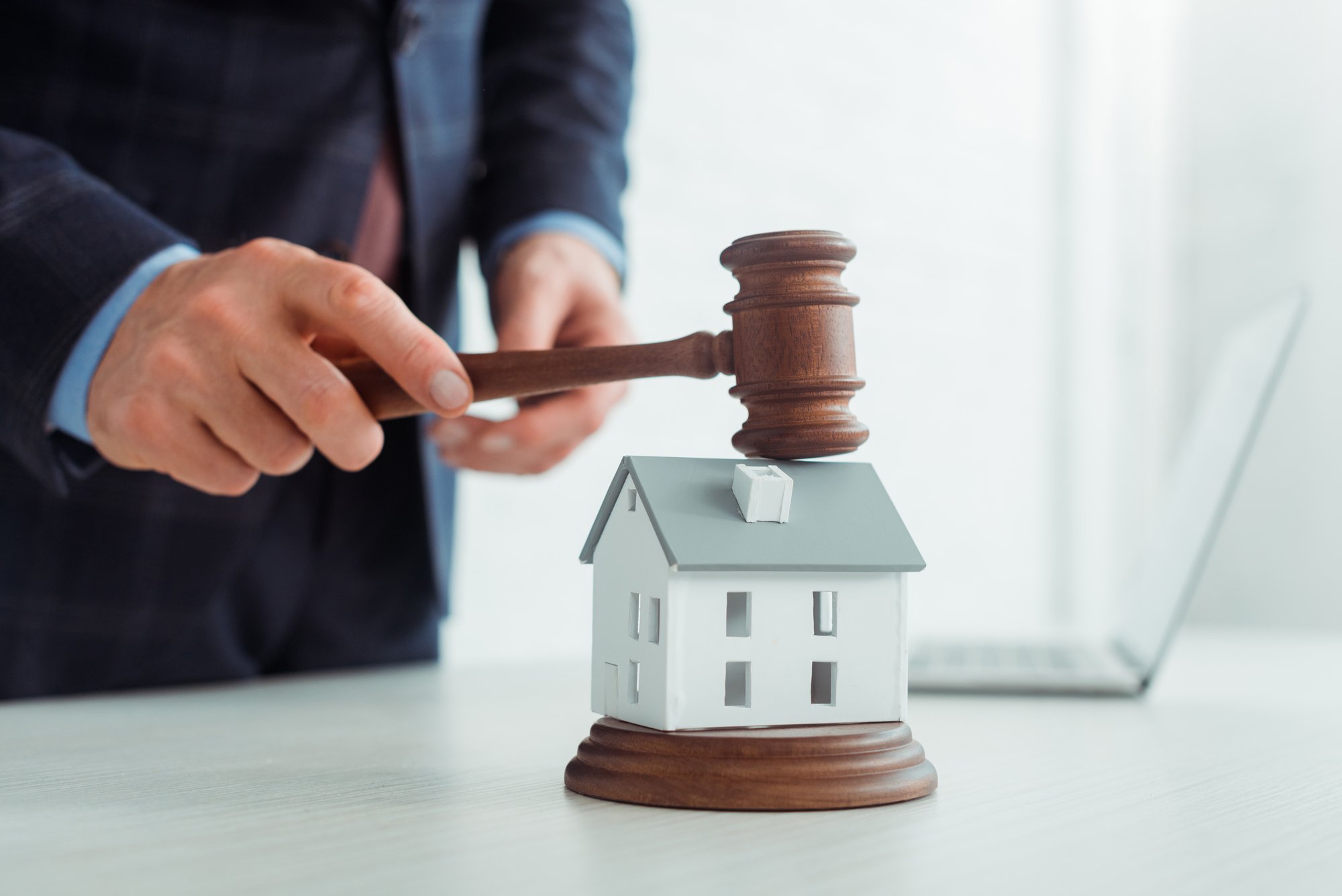 Cropped view of auctioneer hitting model of house with gavel