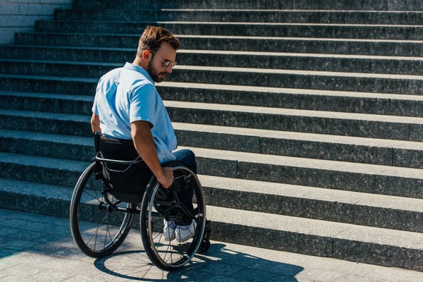 Handsome disabled man using wheelchair on street and stopping near stairs without ramp