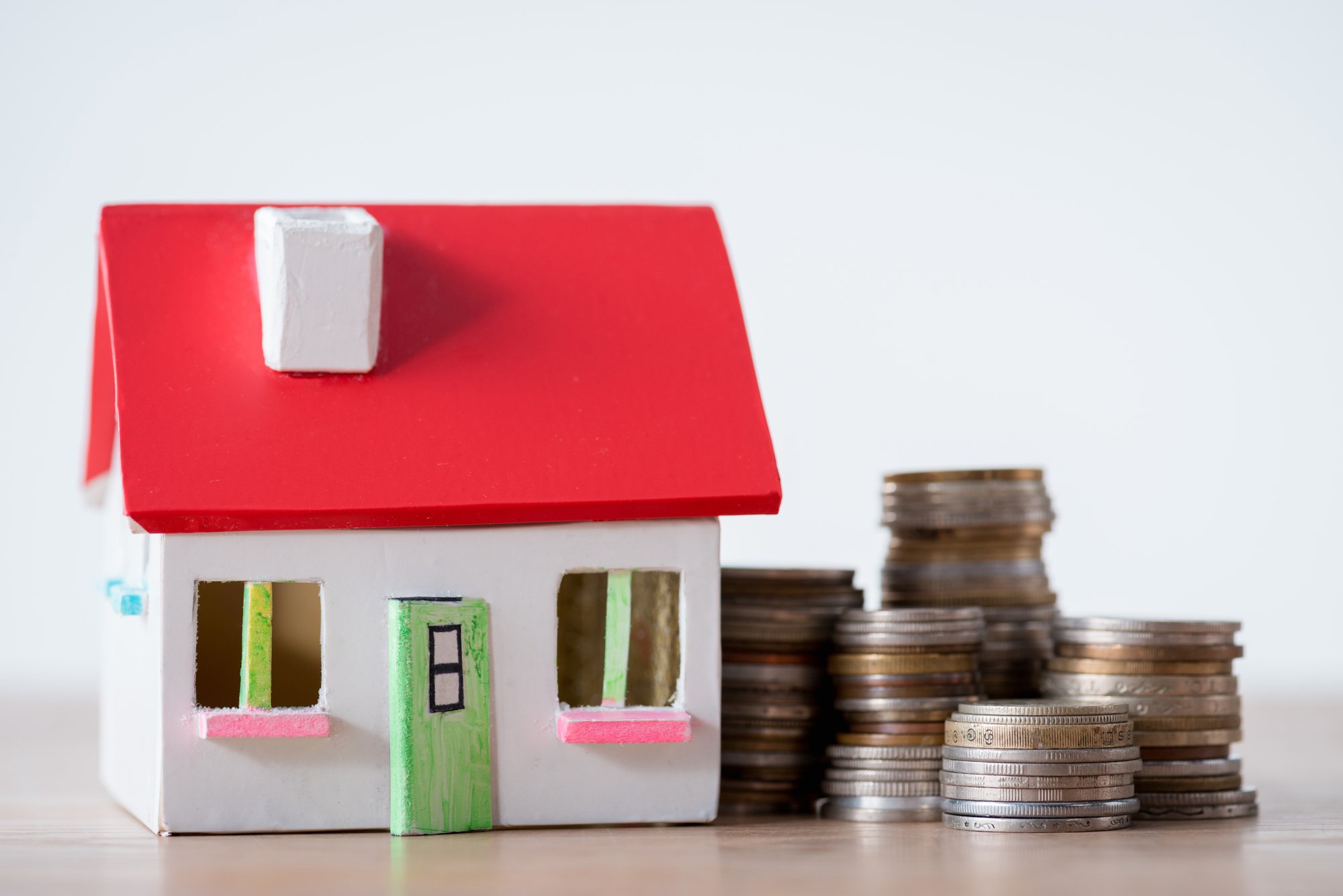 House model with red roof and white walls and stacks of metal coins isolated on grey