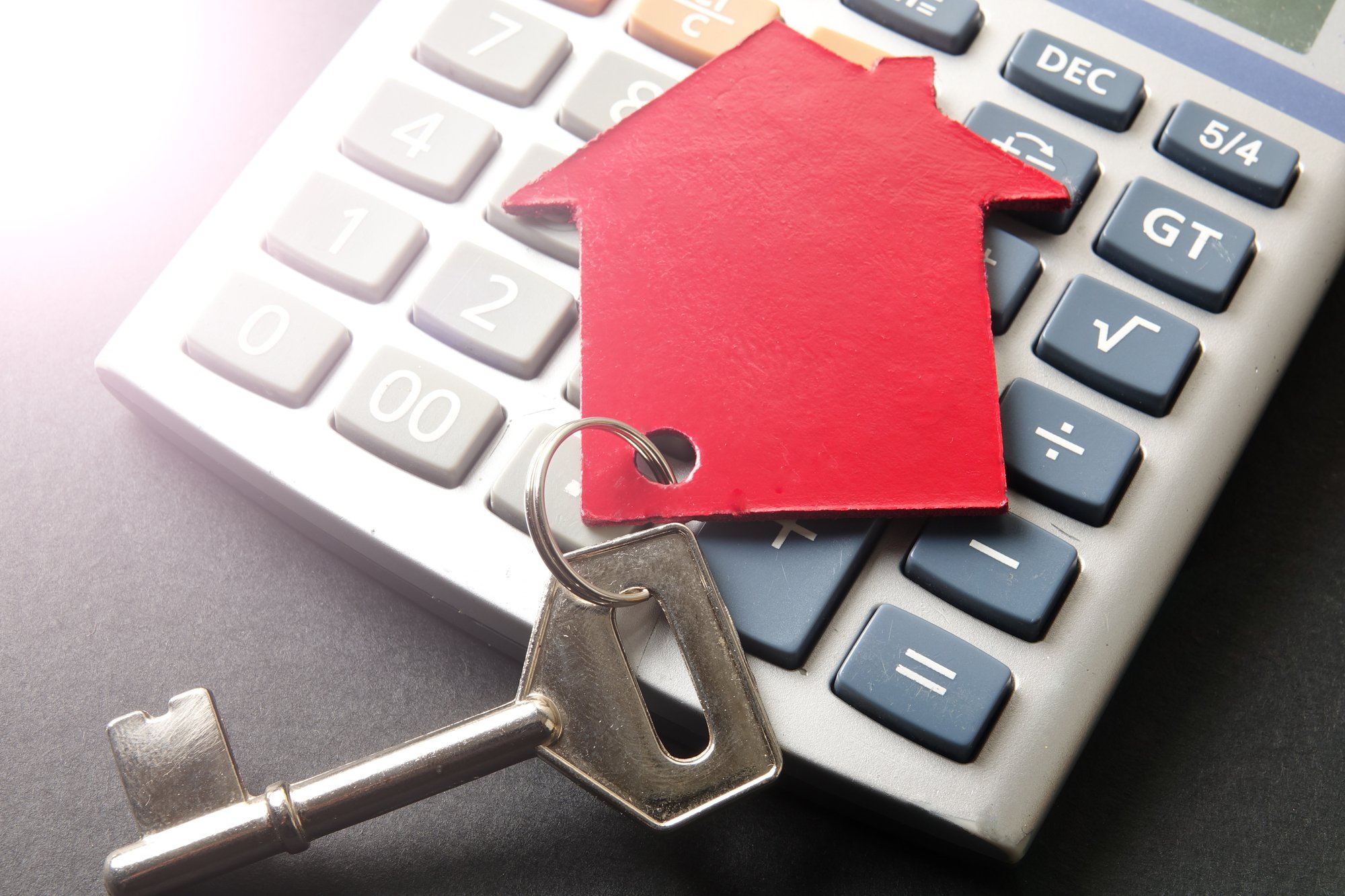 Red small house and steel key on calculator over black backgroun