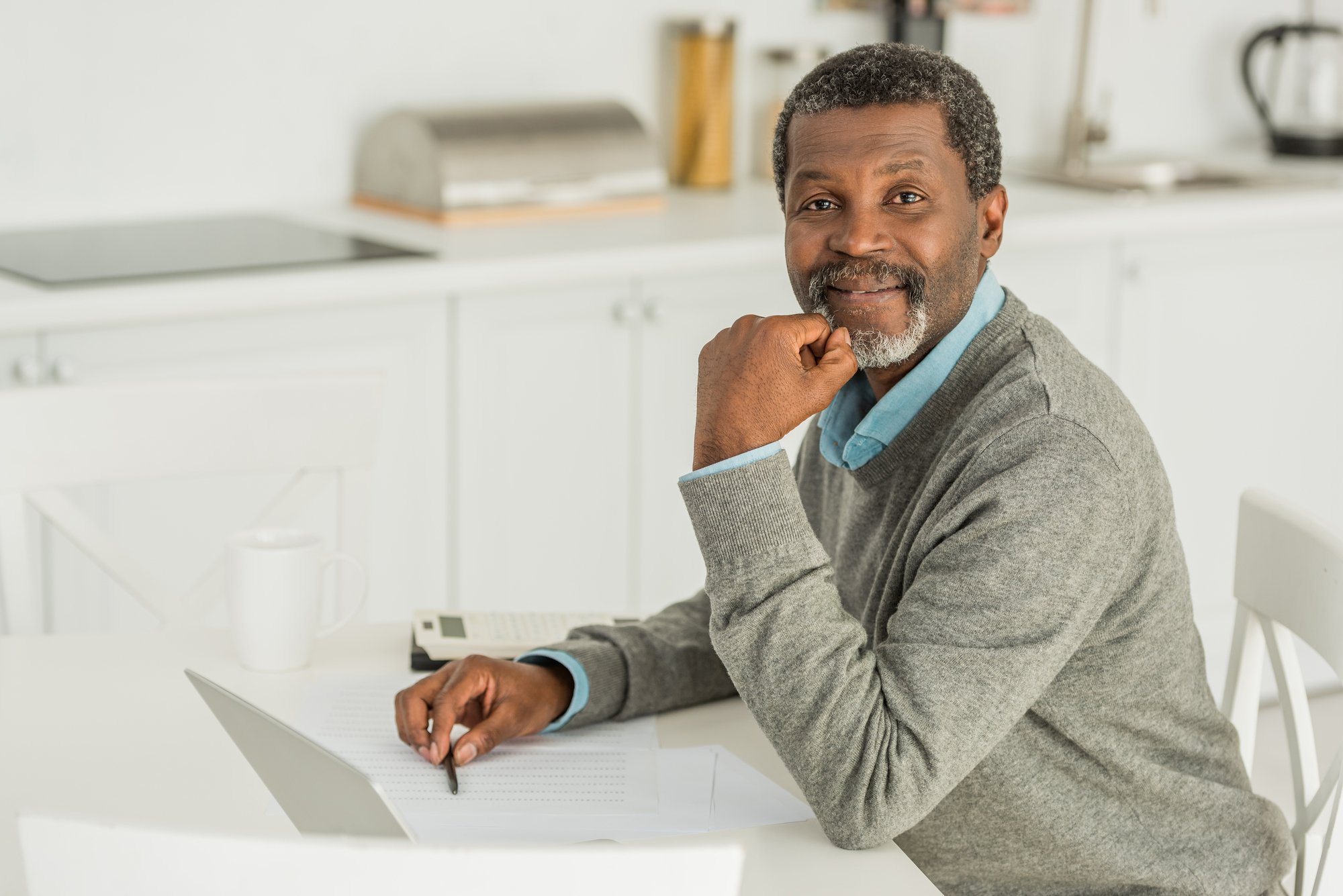 Smiling african american man looking at camera while sitting at table near laptop