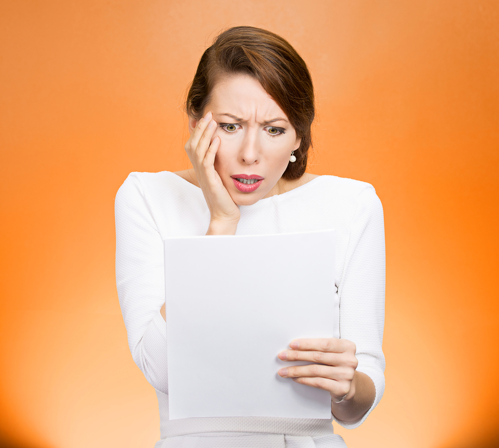 Closeup portrait shocked, funny looking young woman, disgusted at monthly statement, test, application, results isolated orange background. Negative human emotion, facial expression, feeling. Bad news