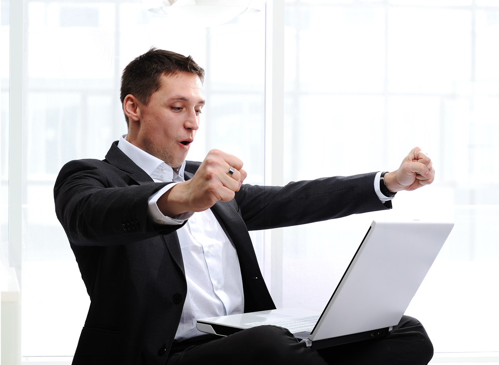 Happy executive raising fists in excitement, in front of laptop