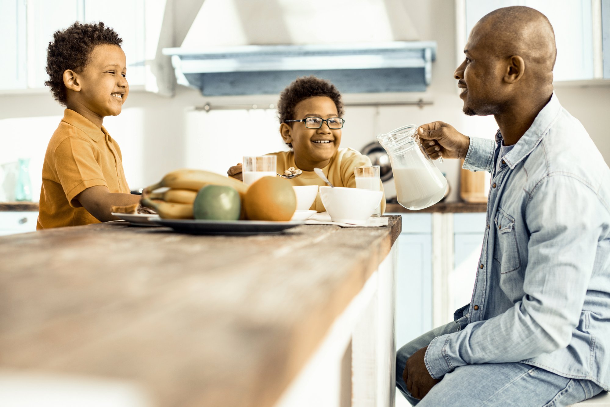 Three - two boys and man - sitting at the table, having lunch and laughing