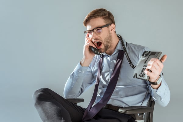 Young annoyed businessman yelling while talking on phone isolated on grey