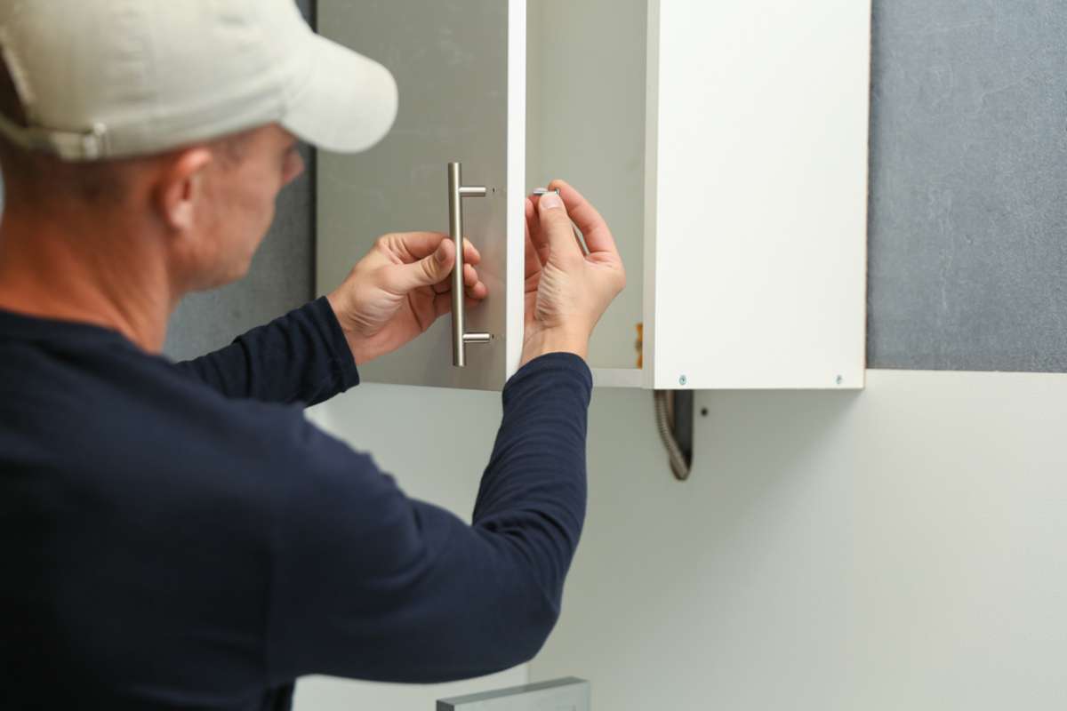 worker installs furniture door handle on the kitchen cabinet.