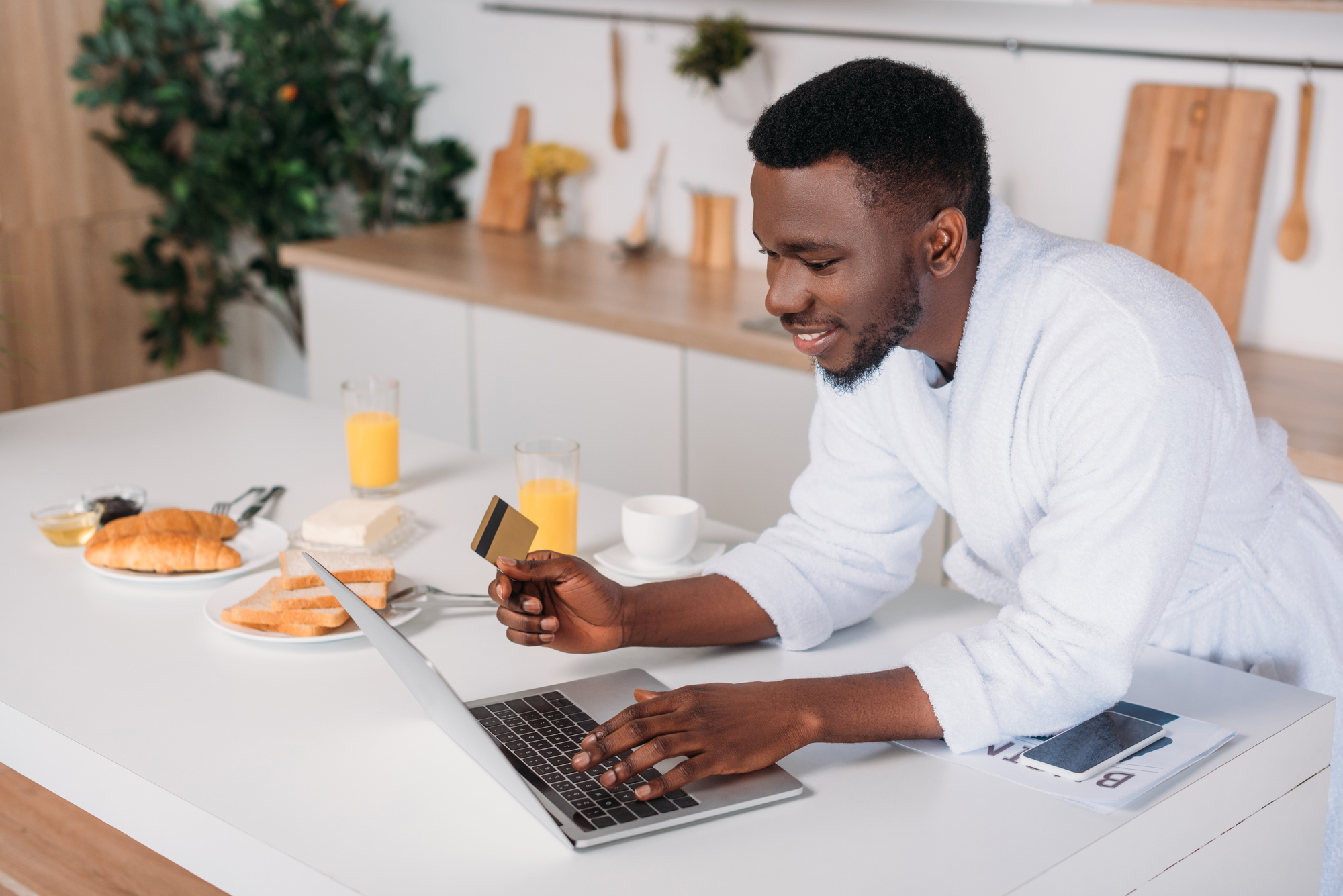 African american man doing online shopping and standing with credit card in kitchen