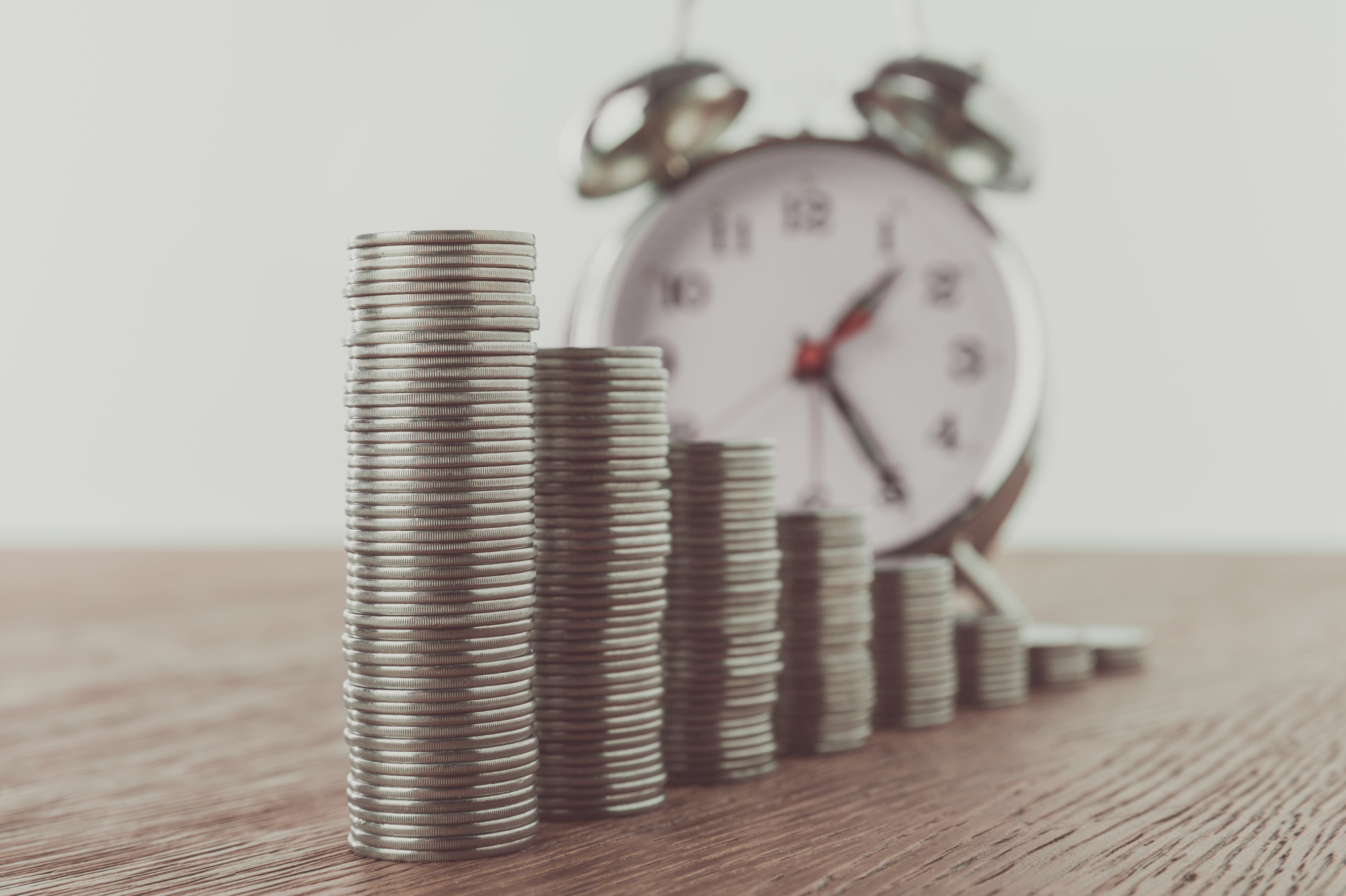 Rising stack of coins with a clock on the background
